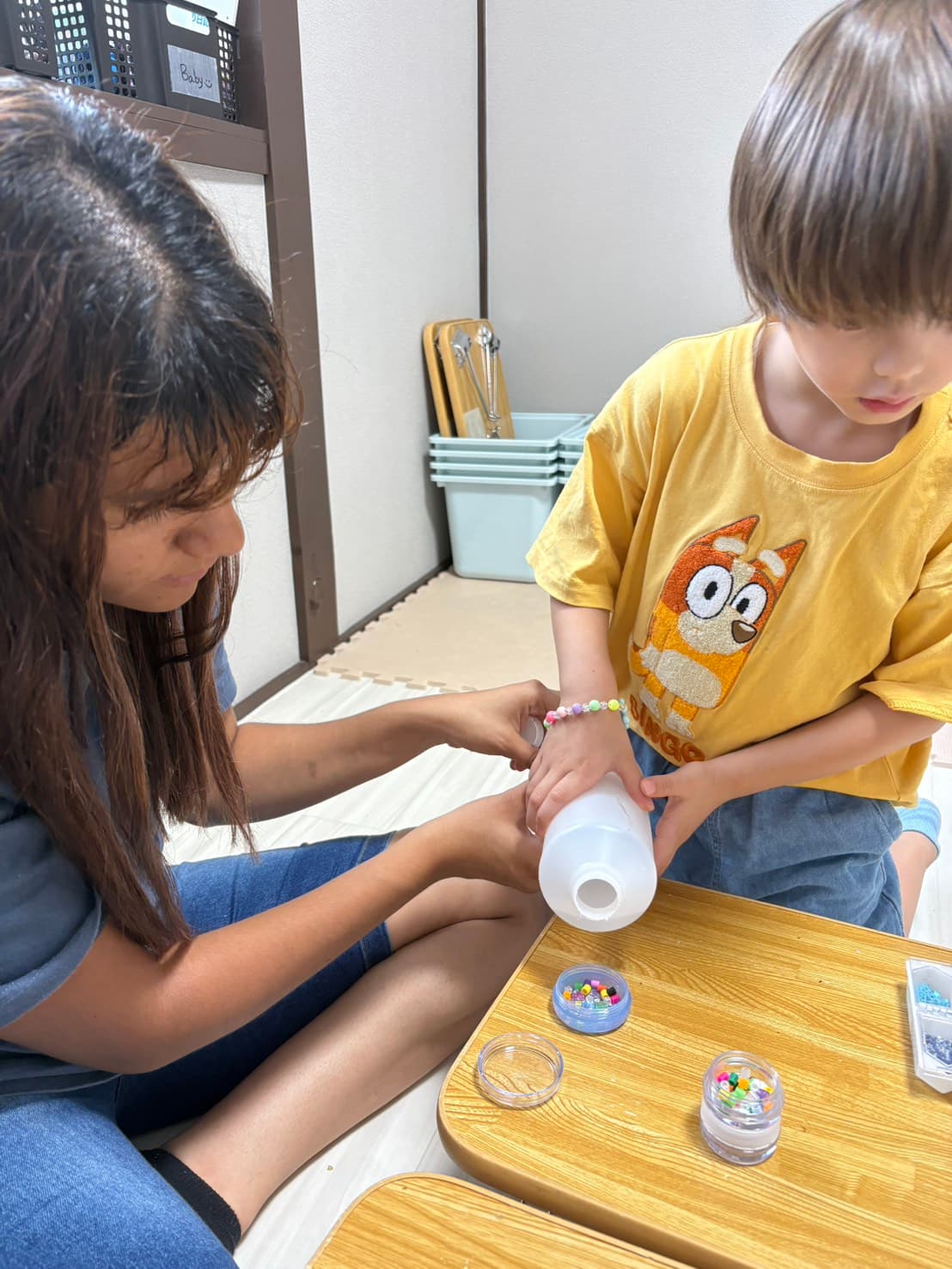 A caregiver and child making a beaded bracelet together
