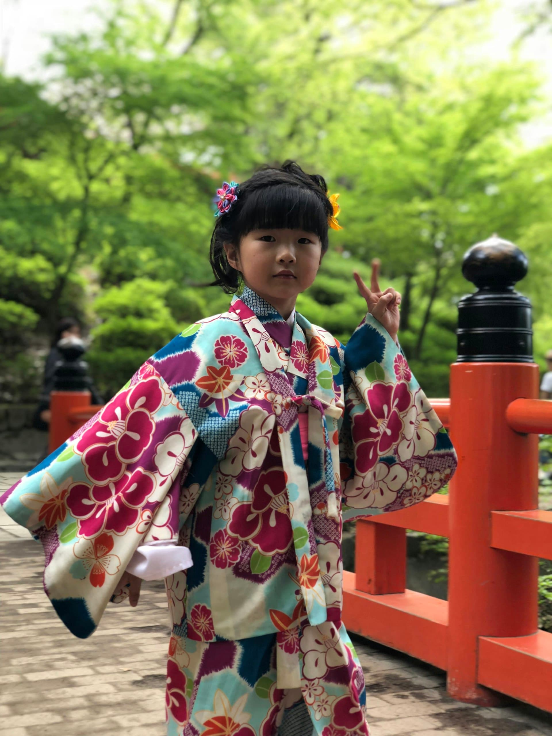 A child in a colourful kimono enjoying a Japanese garden by a vermilion bridge