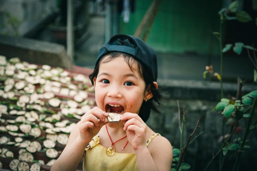 A child smiling while enjoying a snack outdoors